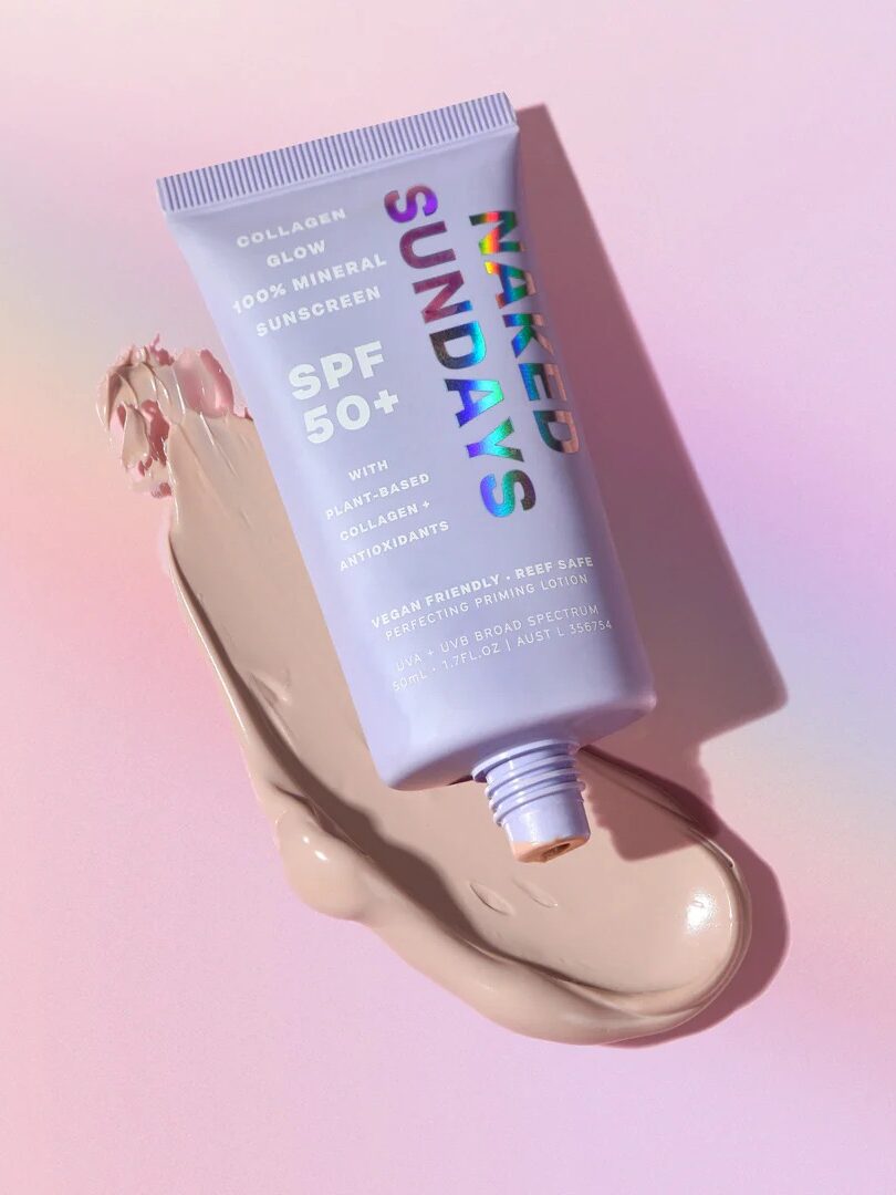 A tube of Naked Sundays SPF 50+ mineral sunscreen lies on a pink surface with product smeared beneath it.