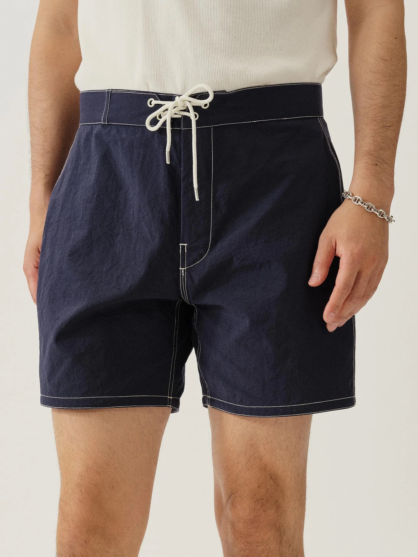 A person wearing navy blue drawstring shorts with white stitching and a white tank top, standing against a plain background.