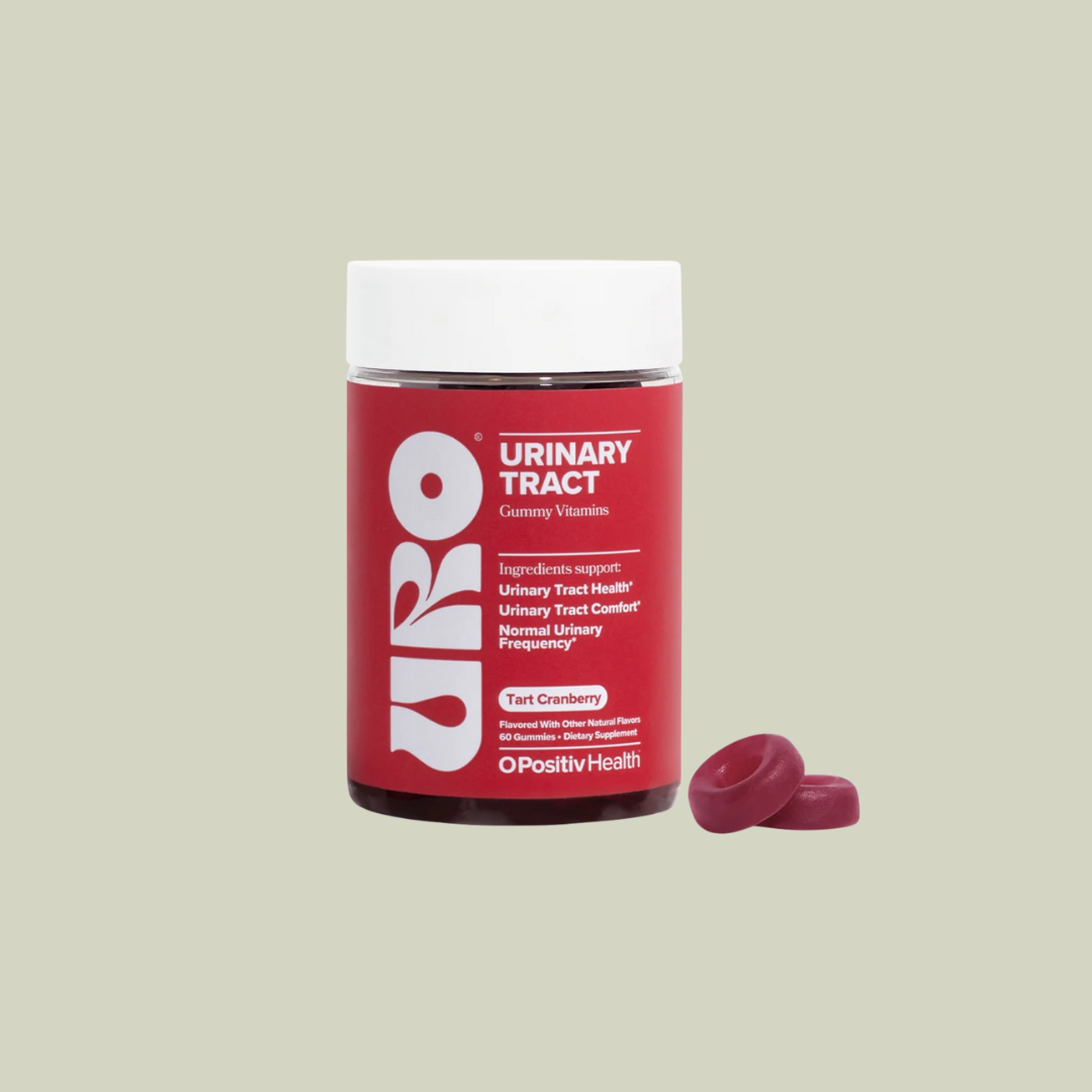 A jar of URO Urinary Tract gummy vitamins labeled "Tart Cranberry" stands next to two red gummies on a light beige background.
