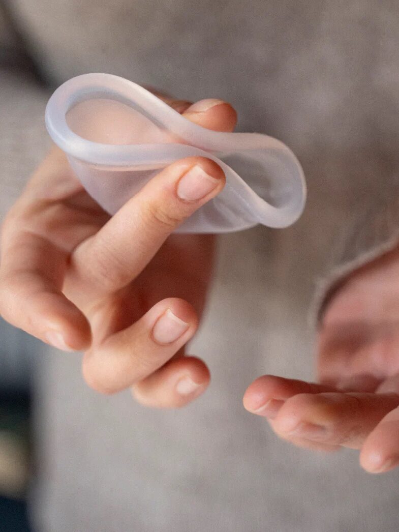 A person holding a folded menstrual cup between their fingers.