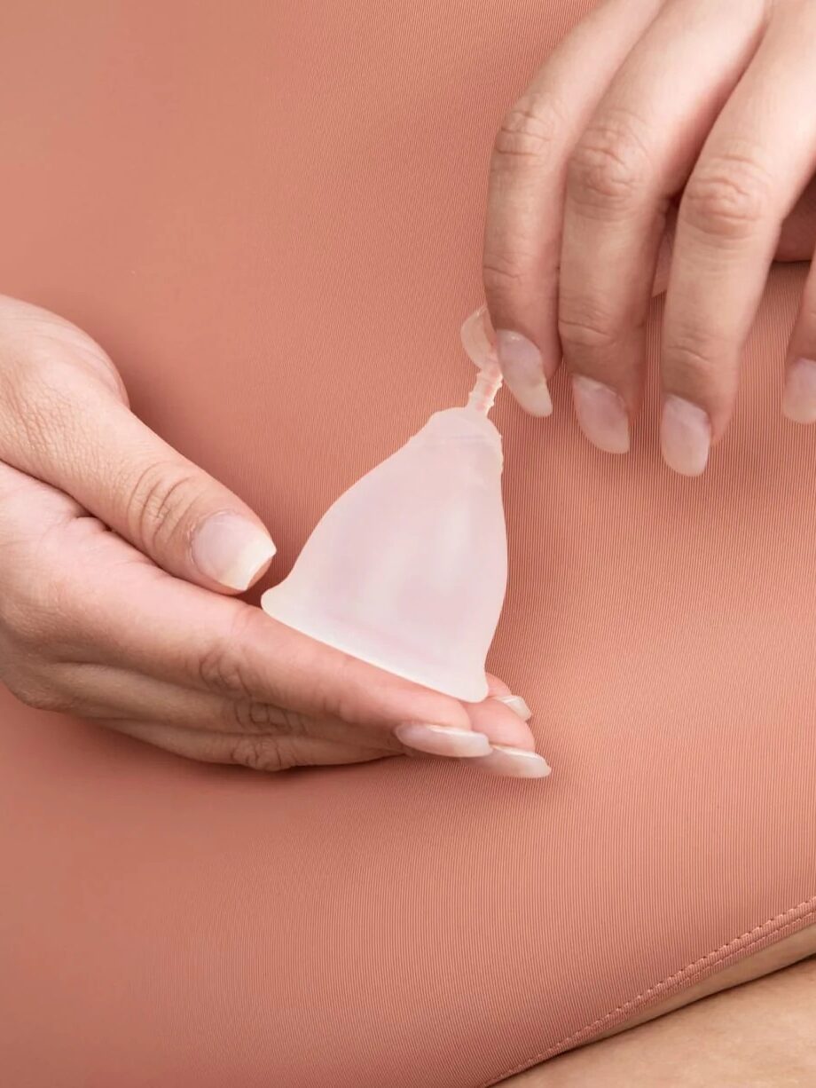 A person holds a menstrual cup against their lower abdomen with both hands, demonstrating menstrual care.