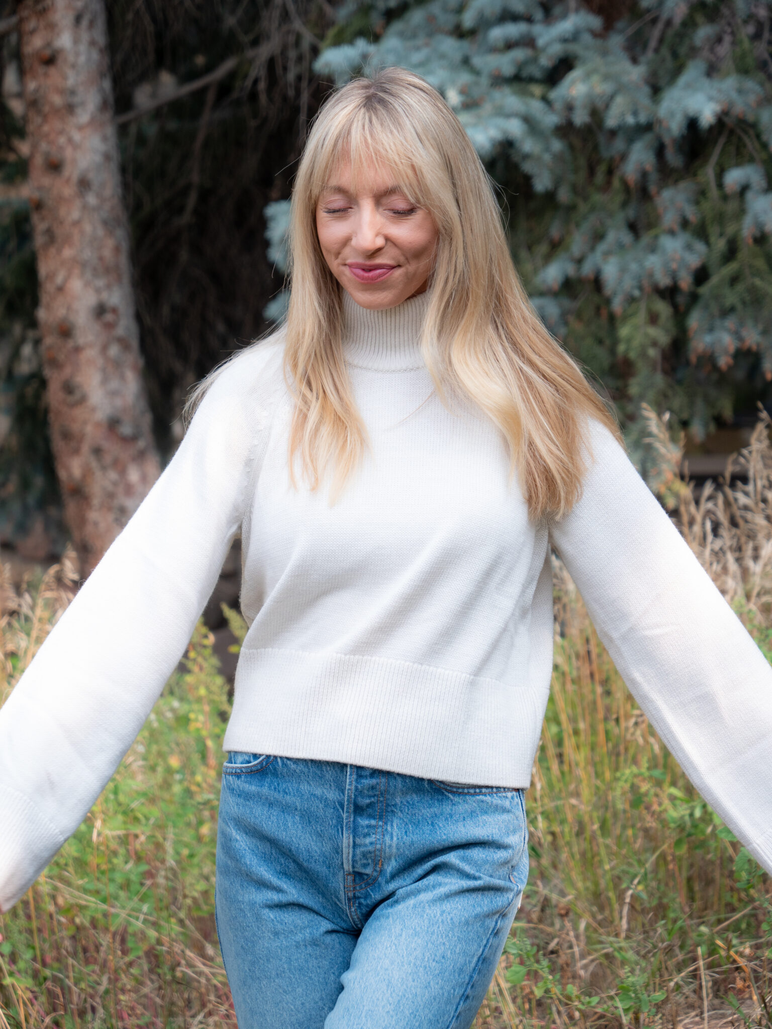 A woman with long blonde hair wearing a white sweater and jeans.
