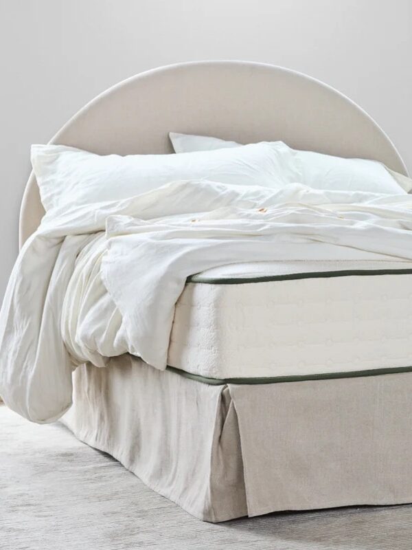 A neatly made bed with white bedding, a rounded upholstered headboard, and an Avocado Green mattress in a bright, minimal bedroom.