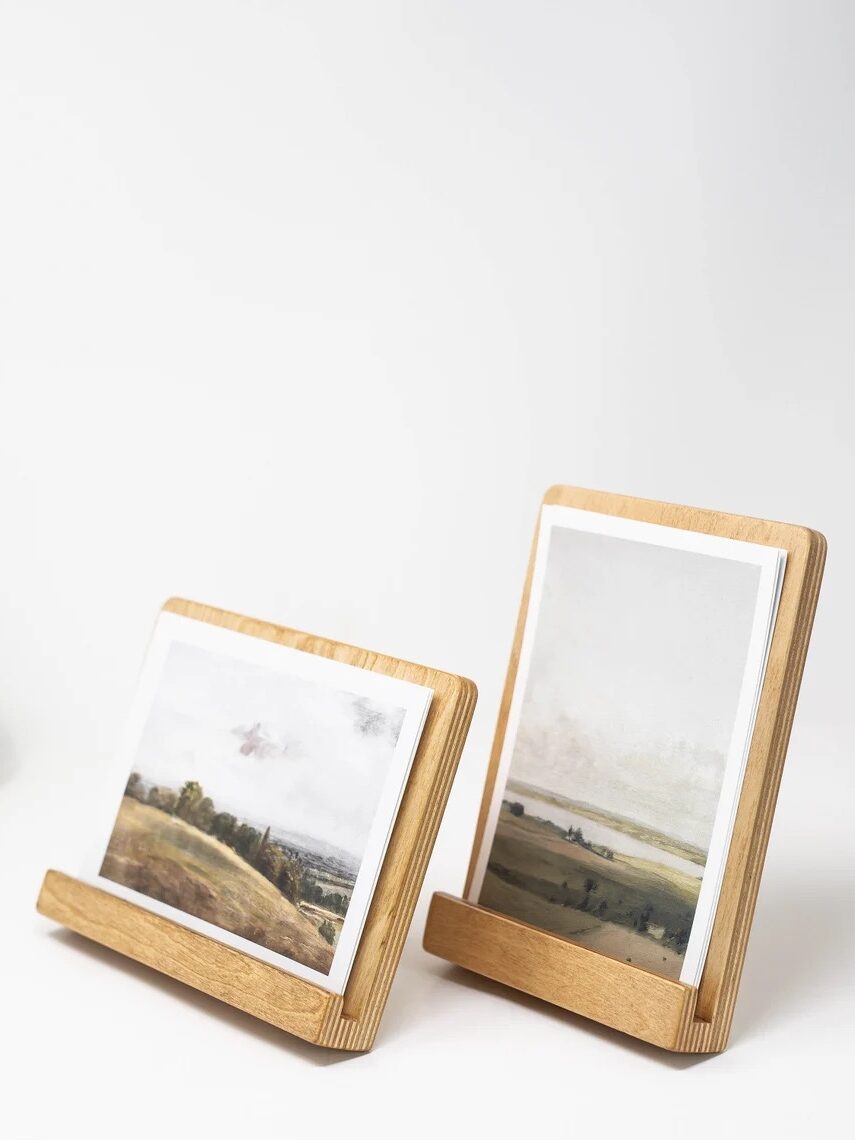 Two wooden photo holders display landscape prints on a white surface, with a decorative pear object blurred in the background.