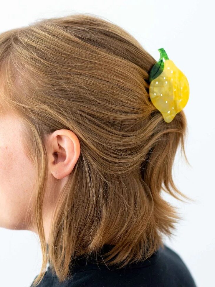 A woman with light brown hair is shown in profile, wearing a lemon-shaped hair clip on the back of her head.