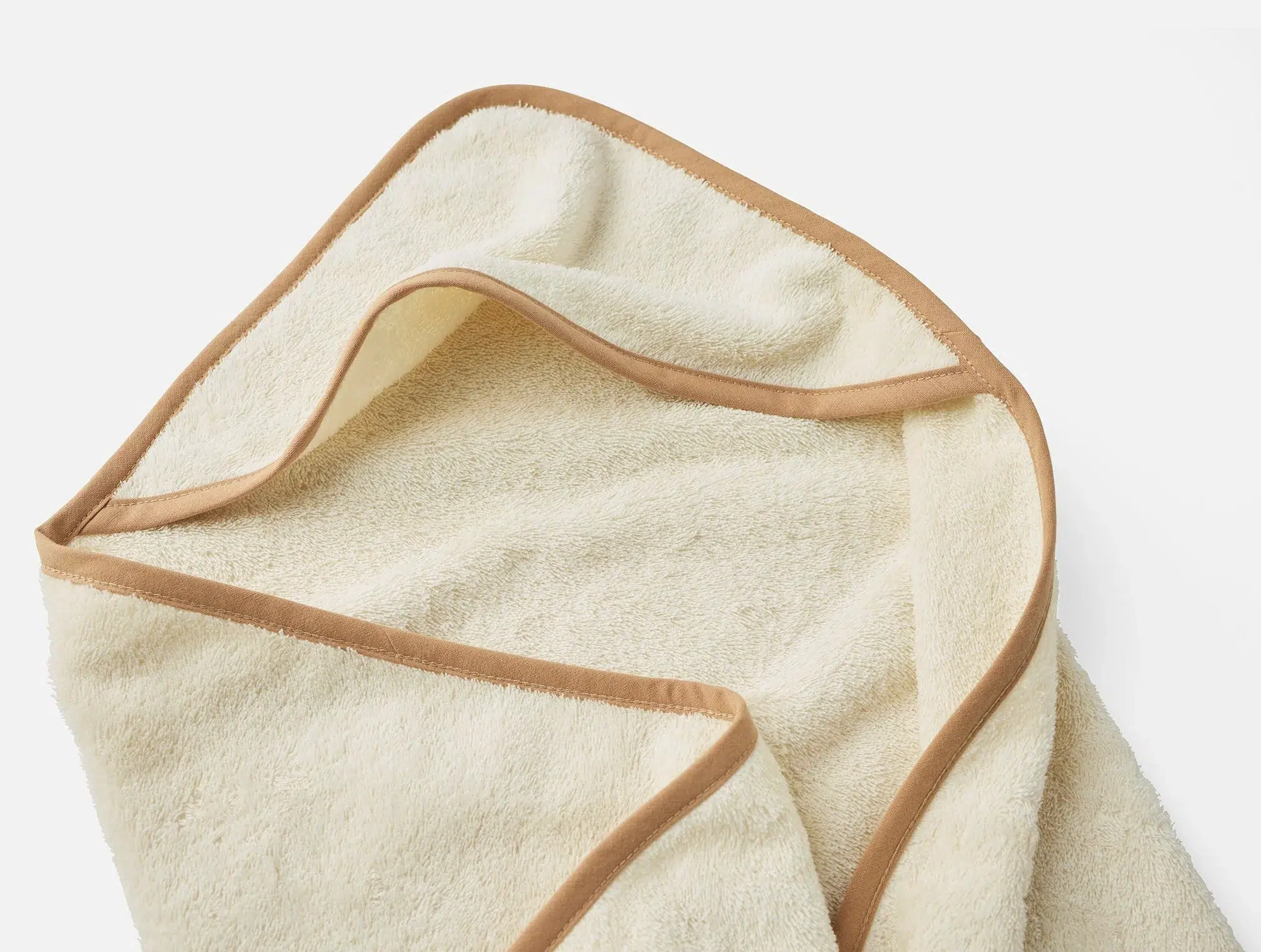 A beige towel with brown trim edges is laid flat on a white surface, with one corner partially folded over.