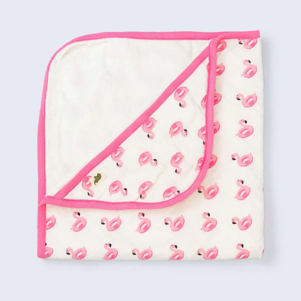 A white baby blanket with pink trim, featuring a pattern of pink flamingos and one gold flamingo, folded with one corner turned down.