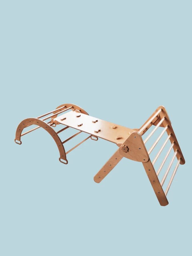 A wooden climbing structure for children with a ladder, an arch, and a ramp, set against a light blue background.