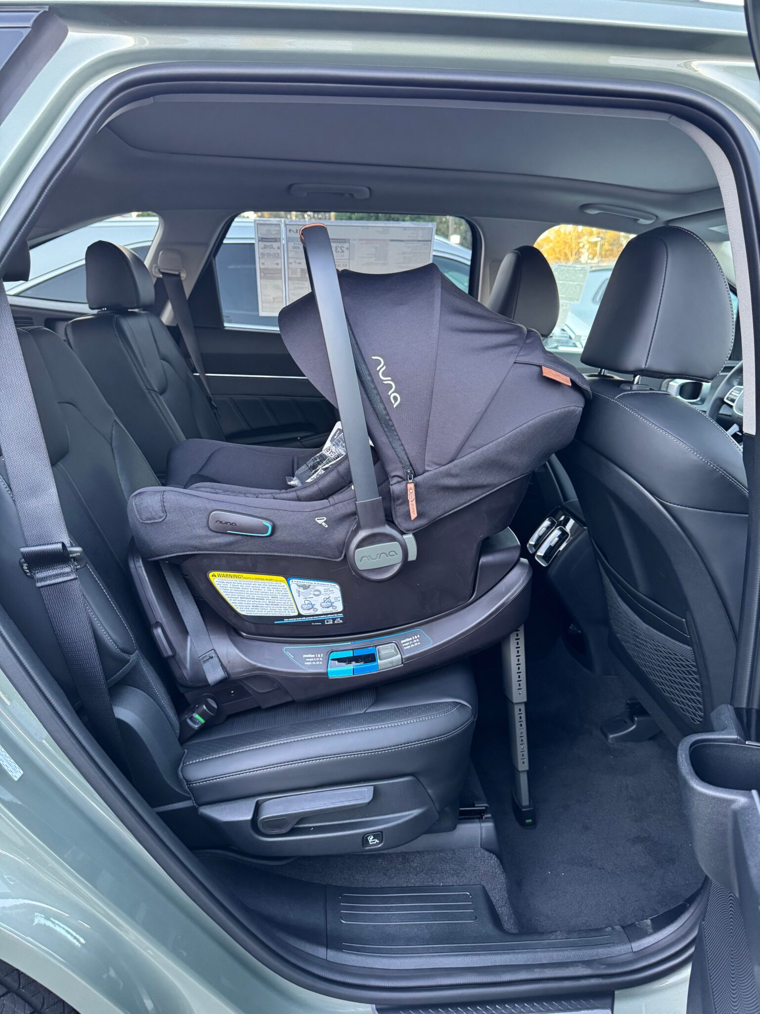 Rear-facing infant car seat securely installed in the back seat of a vehicle, viewed from the open rear passenger door.