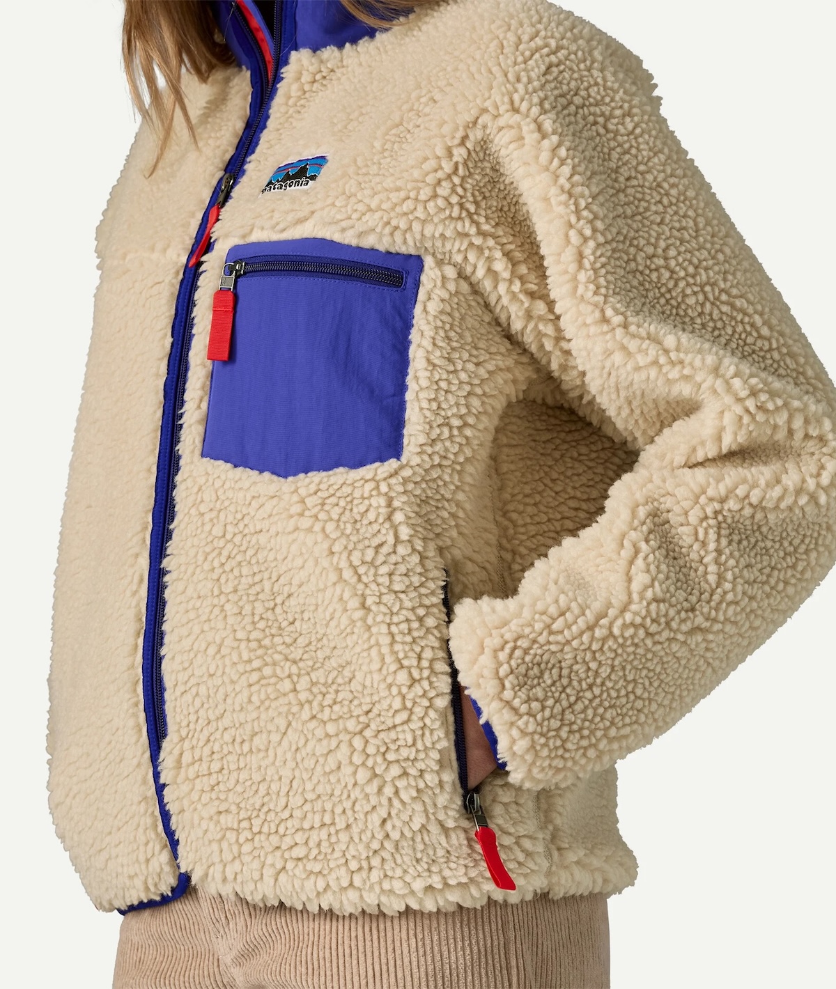 Person wearing a beige sherpa fleece jacket with blue accents and a chest pocket, standing with one hand in the side pocket—a cozy choice inspired by sustainable brands.