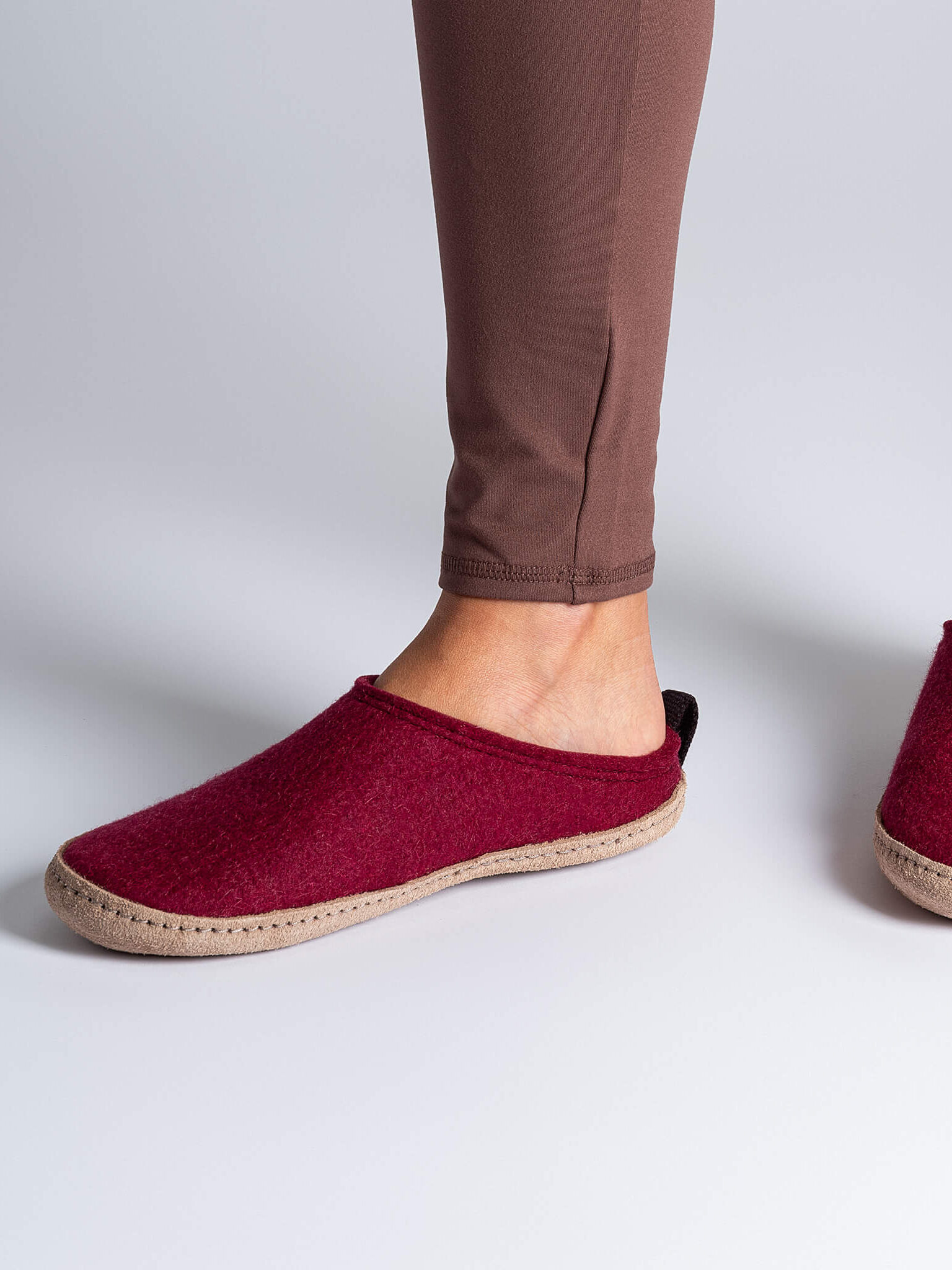 Person wearing brown leggings and cozy red slippers with tan soles, standing on a light grey background.